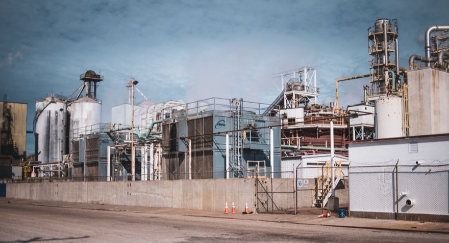 An industrial process plant: tanks, silos, columns and pipework behind the perimeter wall.