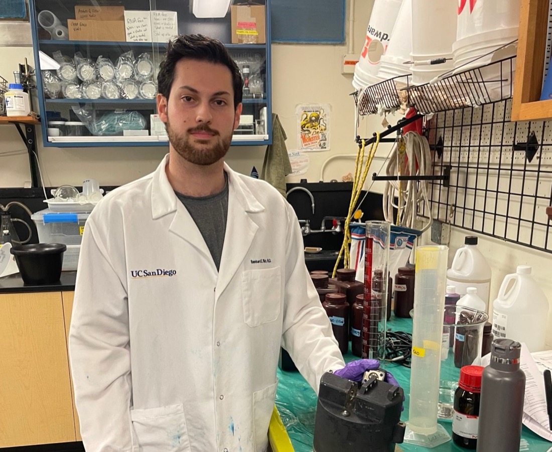 Alex Towfigh in a UC San Diego lab coat beside a sensor housing on the bench.